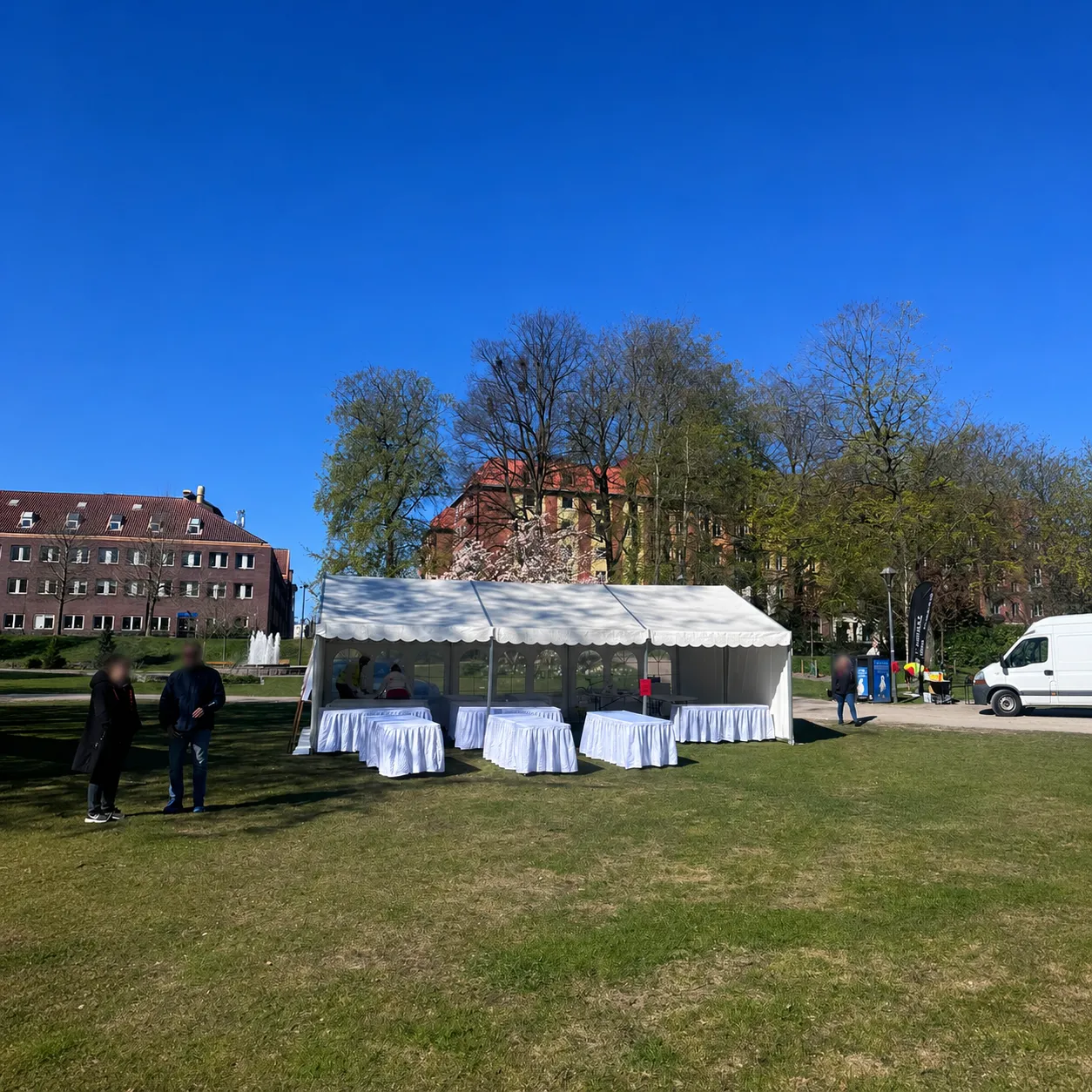 Helvitt partytält 6x9 med bord uppställt i parkmiljö under blå himmel.